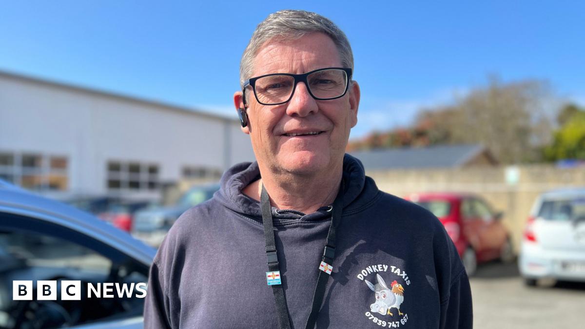 Ian Vaudin pictured with short grey hair wearing black glasses. He is wearing a black hoodie with 'Donkey Taxis' written on the front above a graphic of a donkey and a chicken.