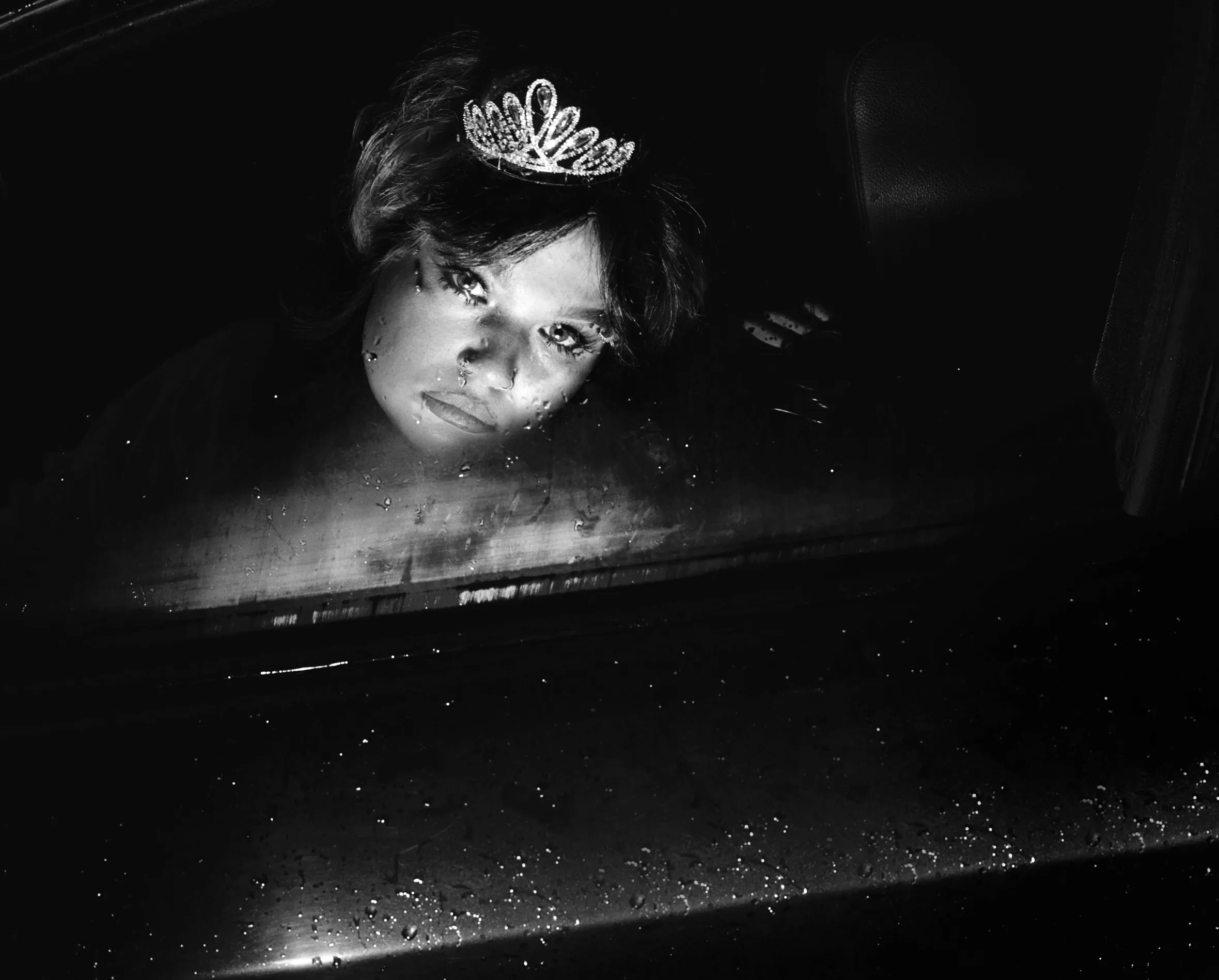 Lola Young wearing a tiara, photographed through a wet car window.