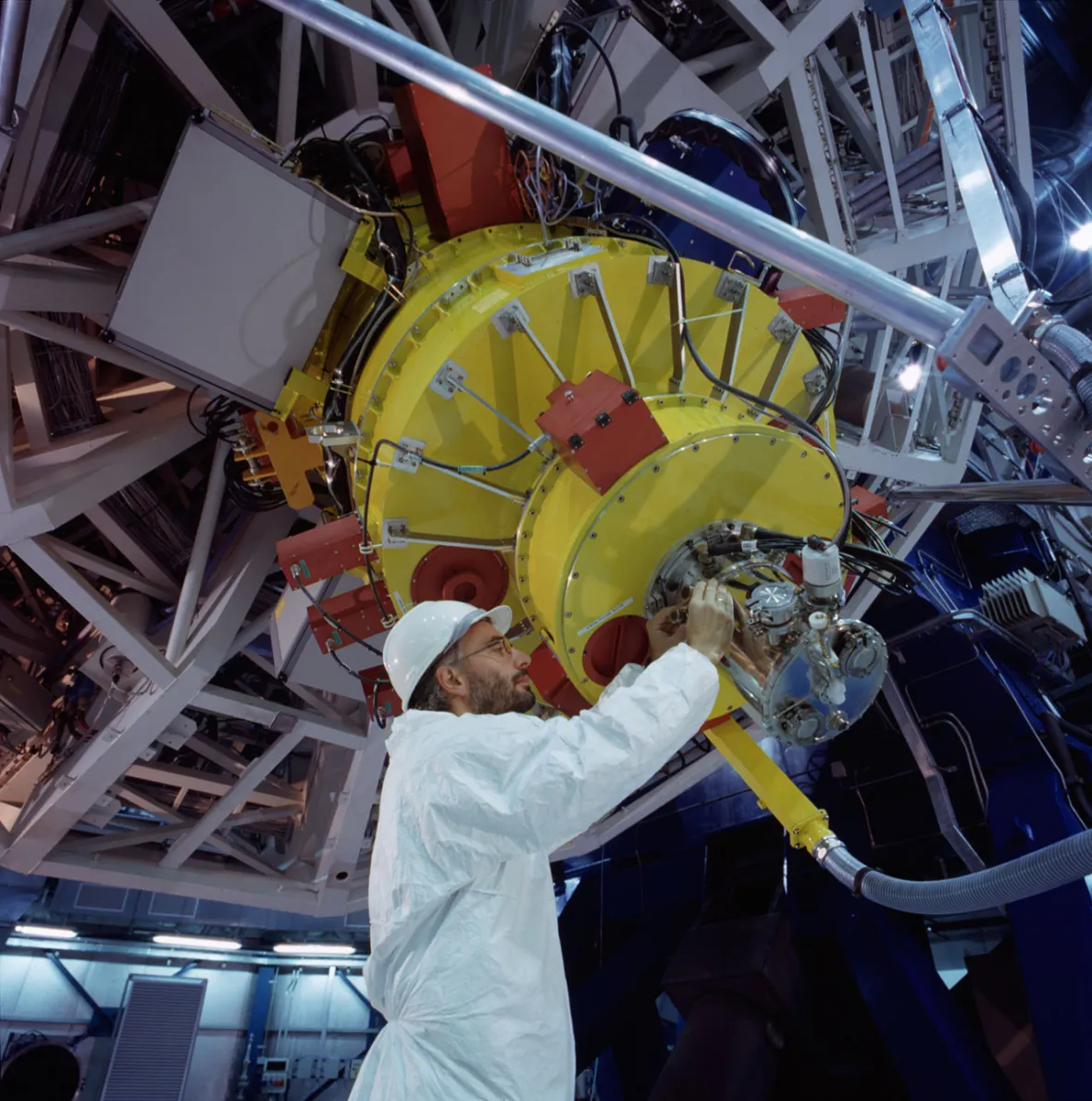 A man in a white lab coat and hard hat working on the FORS2 instrument of the Very Large Telescope.