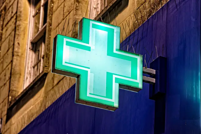 Warminster, Wiltshire, UK - December 29 2022: An illuminated Green First Aid Cross Sign on the facade of Boots the chemist in the Warminster, England