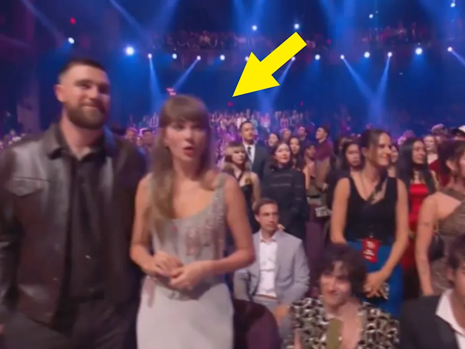 A celebrity is seen in a stylish dress at an award show audience with a crowd of onlookers and bright stage lights in the background