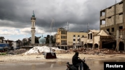 A man drives a motorcycle past the rubble of a site damaged in an Israeli strike in Nabatieh, Lebanon, on March 25.