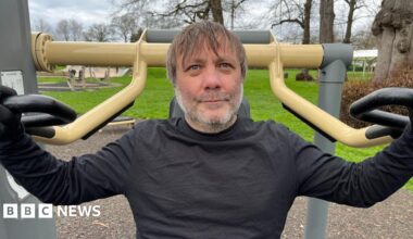 A man sat on a piece of outdoor gym equipment for working out his arms