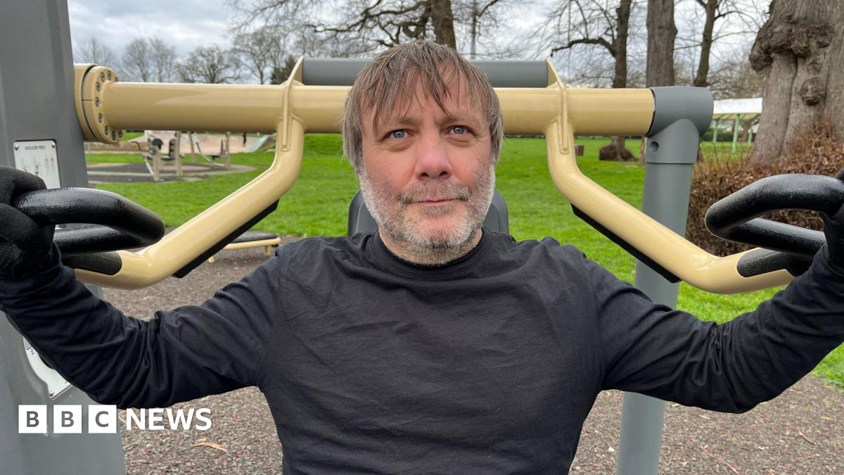 A man sat on a piece of outdoor gym equipment for working out his arms