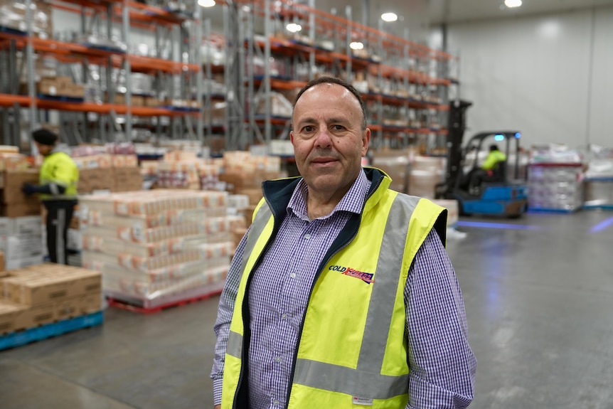 Man in hi-vis yellow jacket smiles at camera inside his warehouse