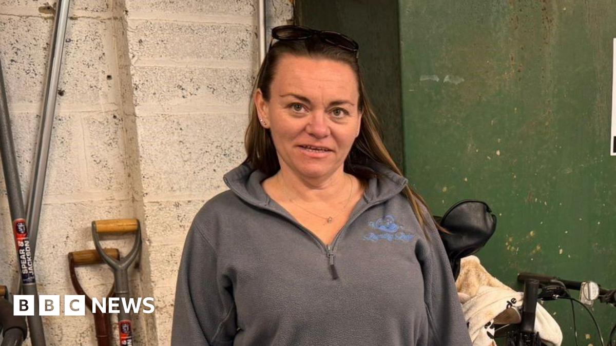 Rachel Douglas is a woman in her 40s wearing a grey top and has long brown hair. She is standing in front of a green tank - on the top is a guage which has an arrow pointing to empty
