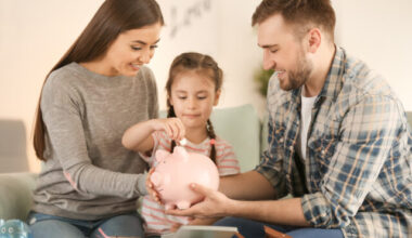 Little girl with her parents sitting on sofa and putting coin in