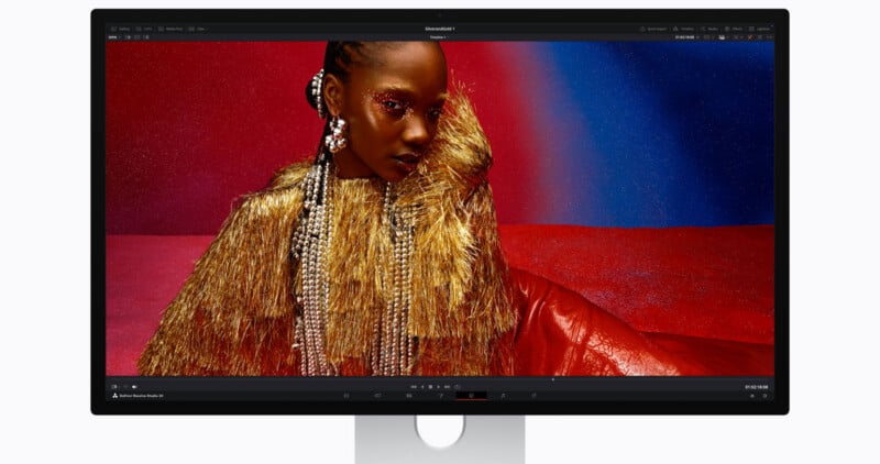A computer monitor displays a vibrant image of a model wearing a gold, fringed outfit and pearl accessories against a bold red and blue background.
