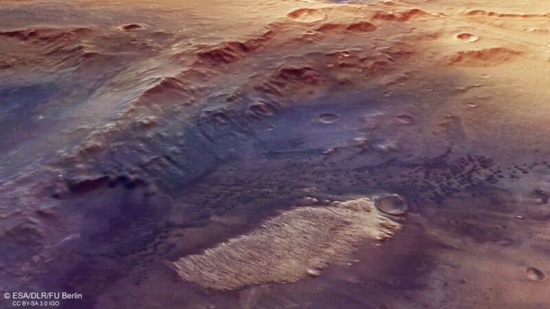 A high-resolution image of a rugged Martian landscape showing cratered terrain, rocky ridges, and elevated plateaus with varying shades of brown, orange, and purple. Image credit: ESA/DLR/FU Berlin.