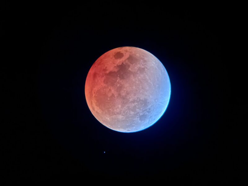 Full moon with reddish tones at upper left and bluish at lower right.