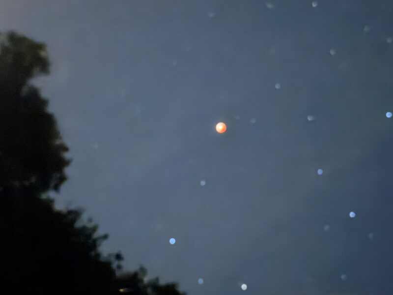 Blurry view of stars and a reddish moon in the night sky.