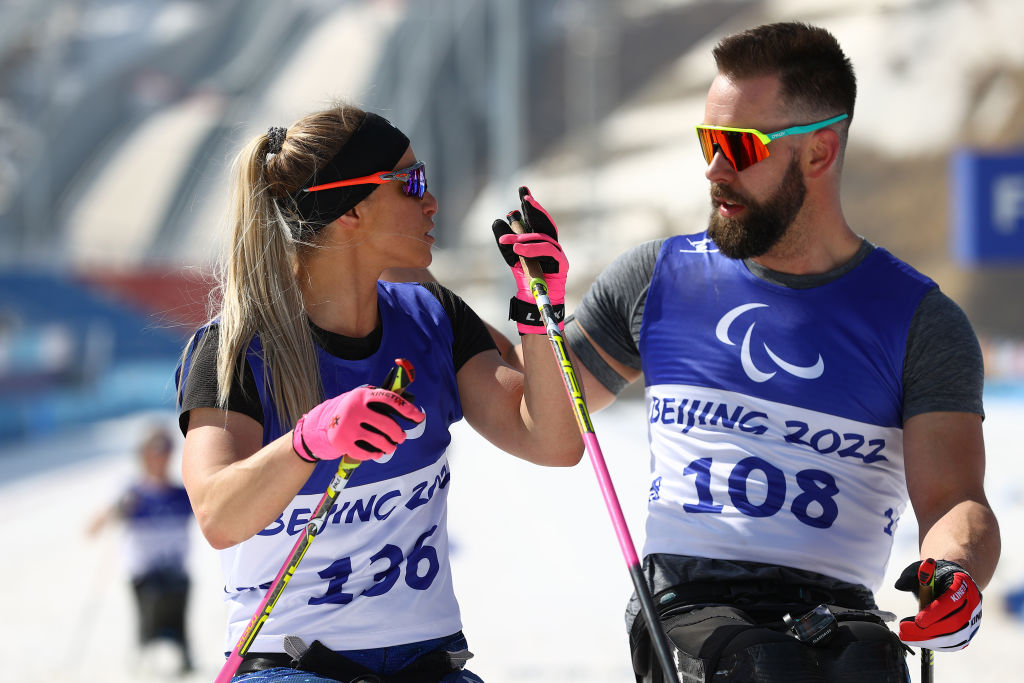 A male and female athletes wearing Beijing 2022 bibs are talking