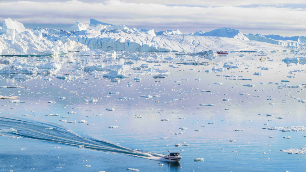 A boat sails through light blue, ice-specked water.