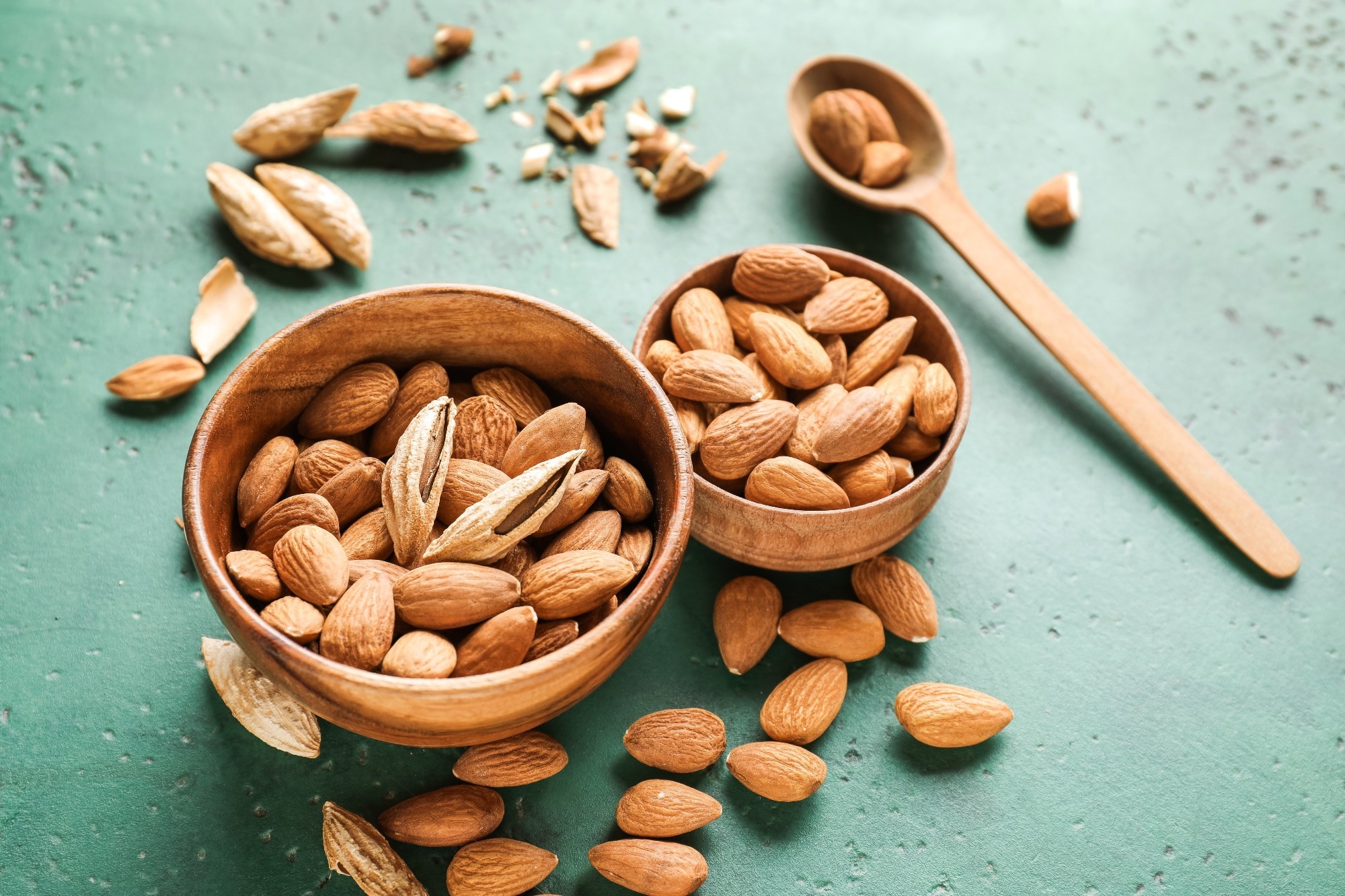 Bowls with tasty almonds on color background