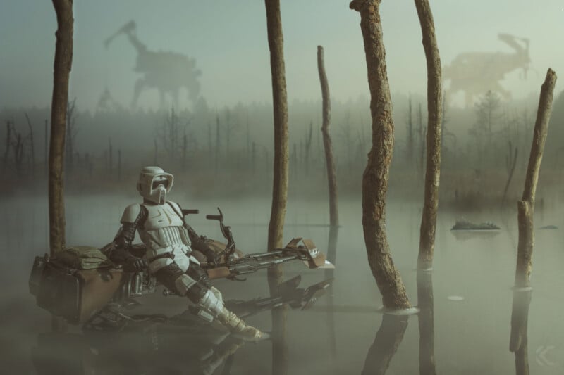 A Star Wars scout trooper sits on a speeder bike in a misty swamp surrounded by trees, while two AT-AT walkers loom in the foggy background.