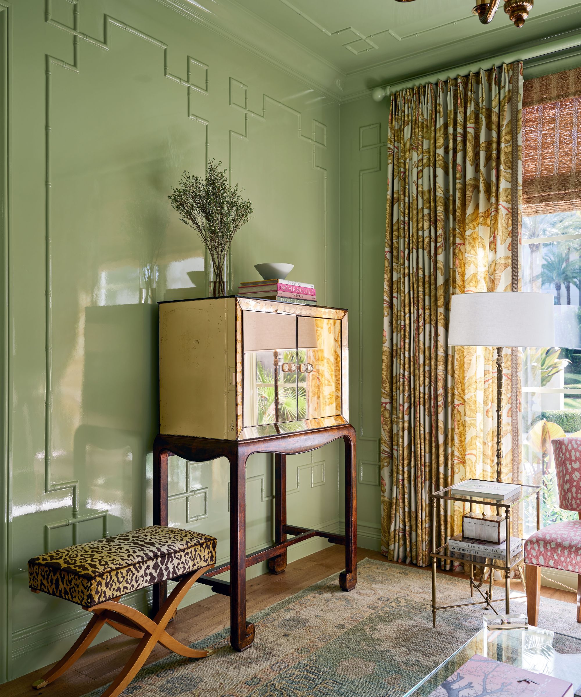 Living room with pale green lacquer walls, mirror drinks cabinet, leopard stool, persian rug and glass coffee table