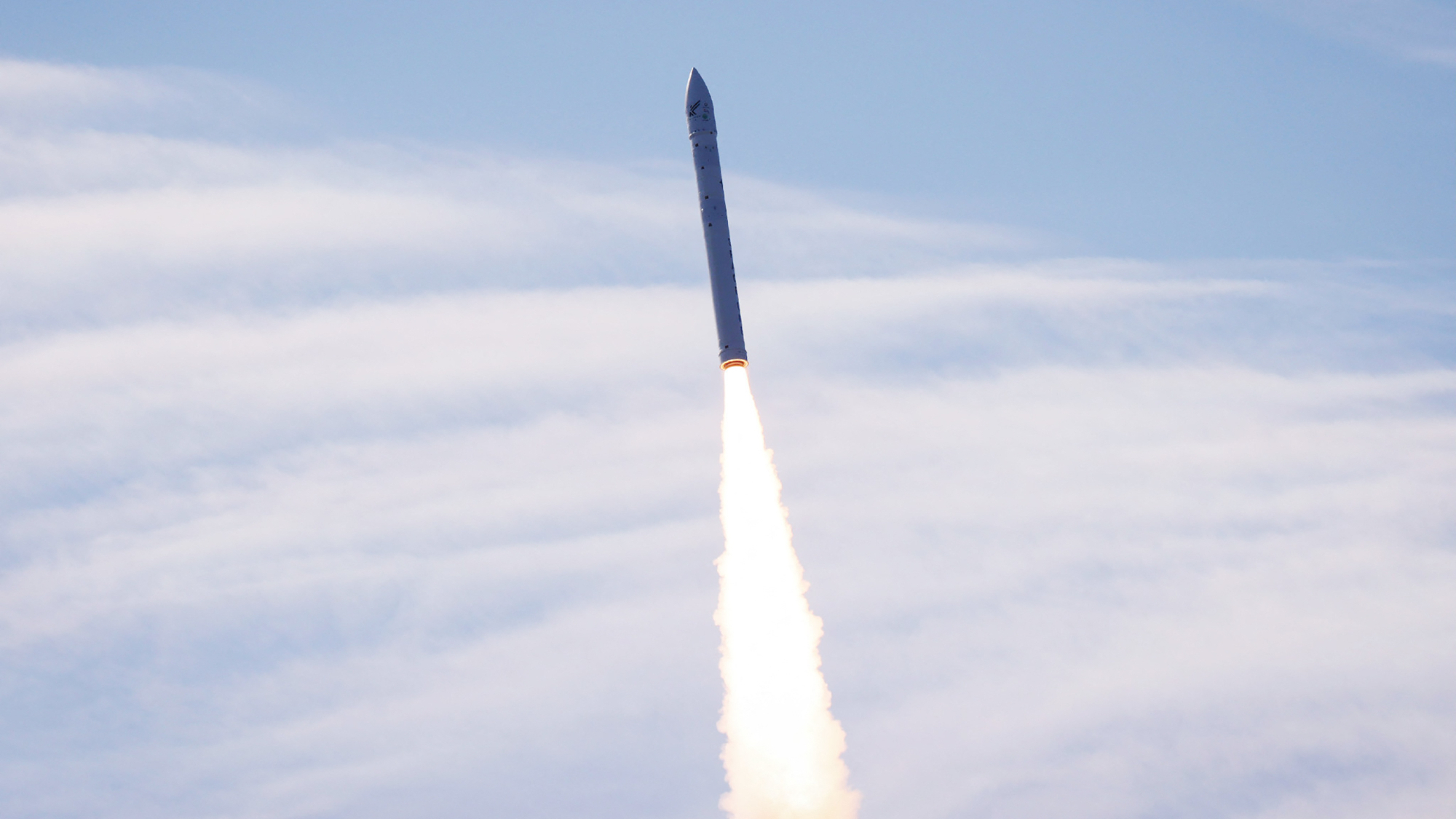 a small white rocket rises into a cloudy blue sky