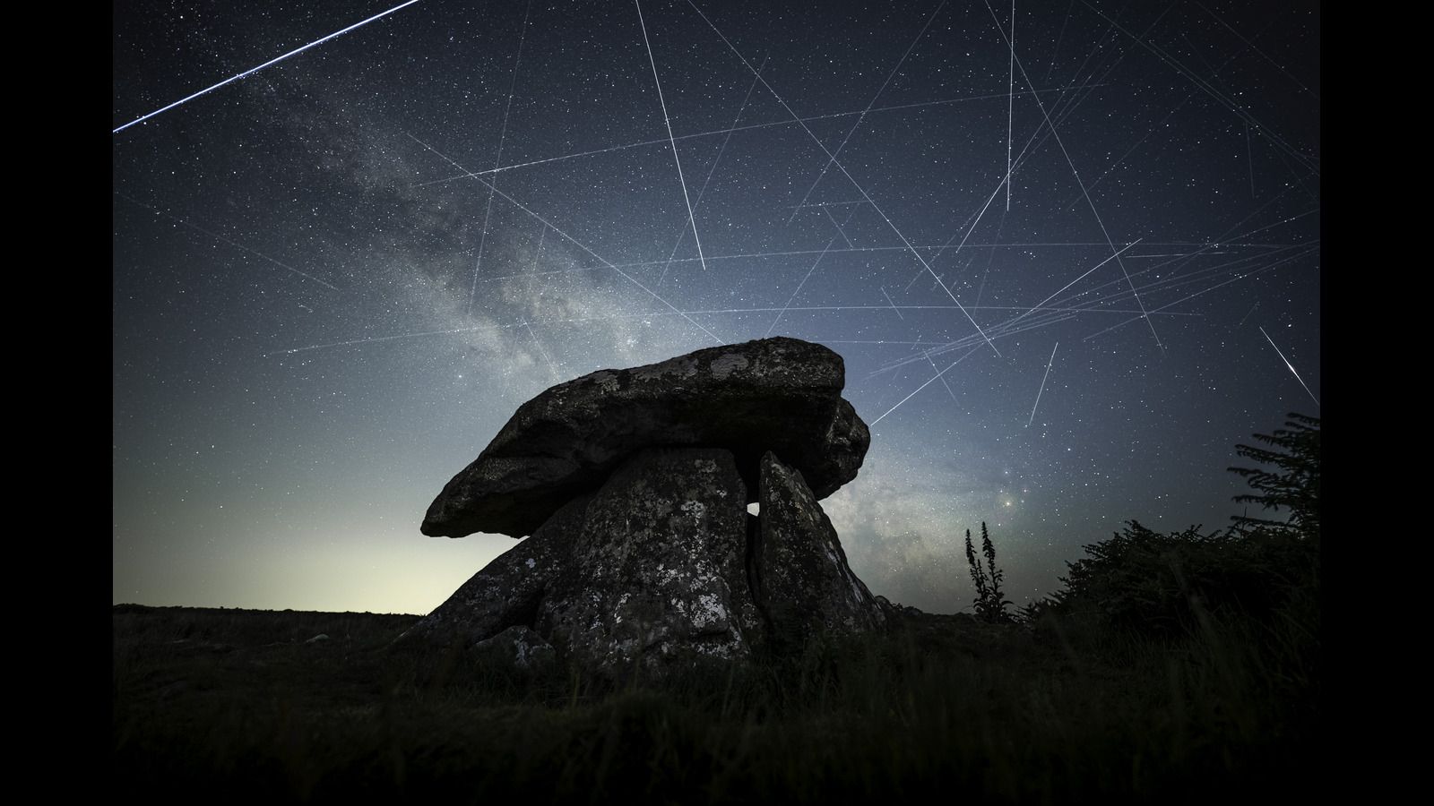 Satellites are pictured leaving long 'trails' in the night sky in a composite image featuring the Milky Way hanging over a stone monument.