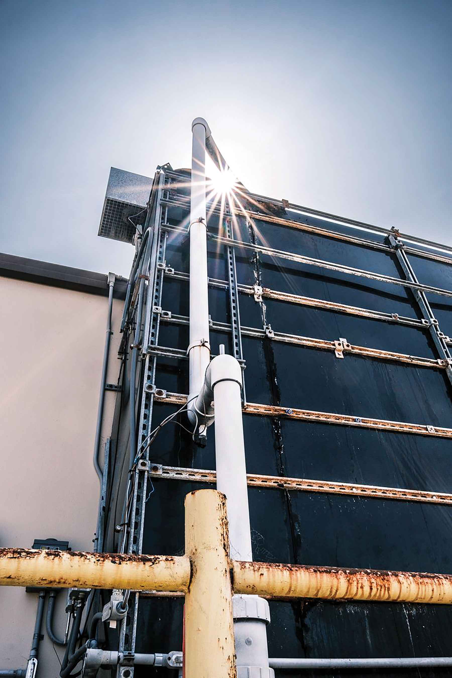 A white pipe runs up the vertical face of a black air contactor, a tall rectangular box, as the sun shines over the top.