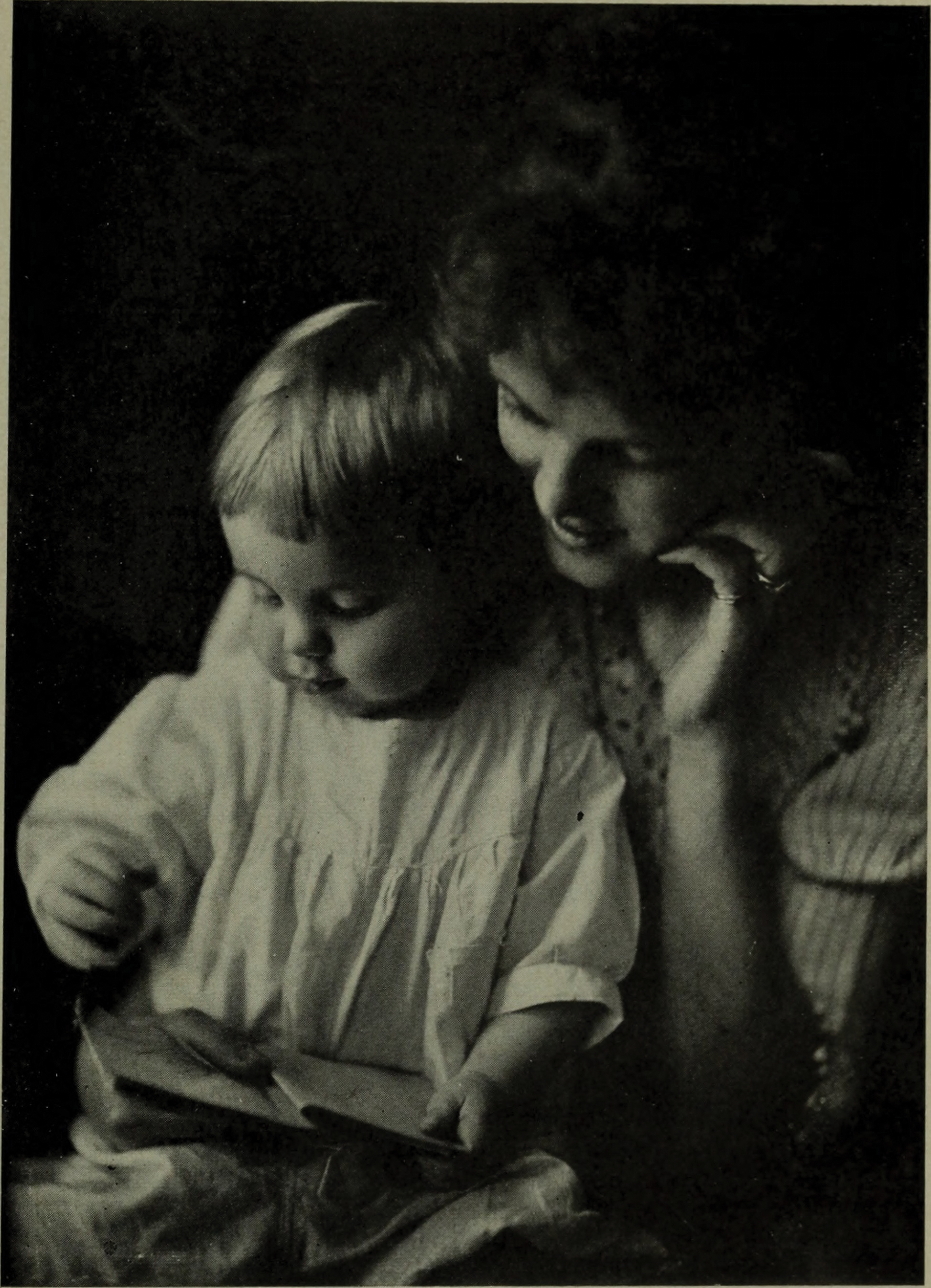 A woman lovingly observes a child reading a book. The child, focused and curious, sits on her lap