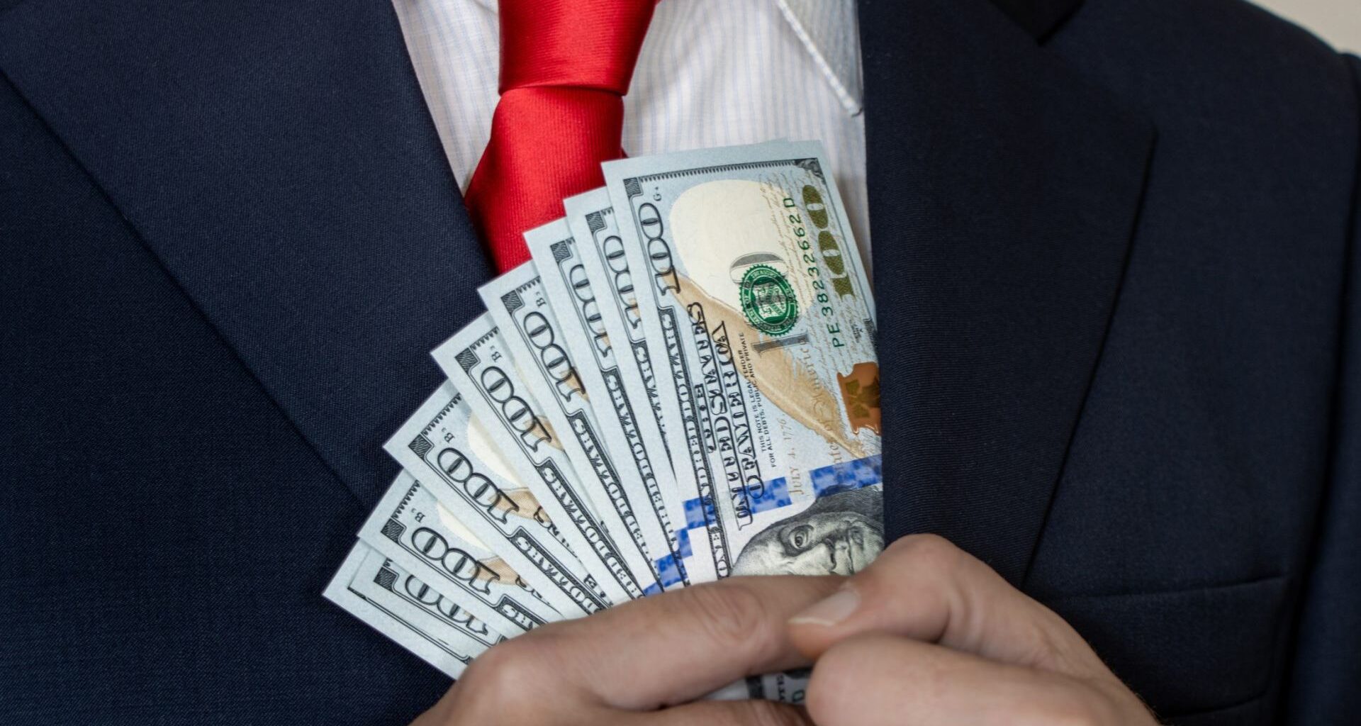 A rich man in a suit and tie counts US dollars in his hand and puts them in his pocket.