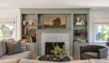 Living room with grey-green painted built-in bookshelves with decor and books, fireplace with a landscape painting above it, neutral sofa, and a dark grey velvet armchair