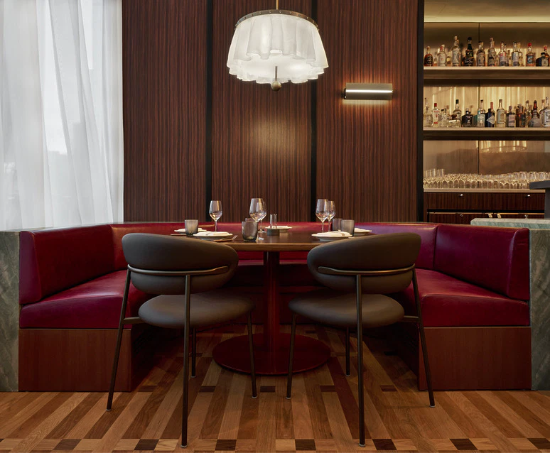 Cozy restaurant seating with red velvet booths, wine glasses on the table, and a stylish chandelier above.