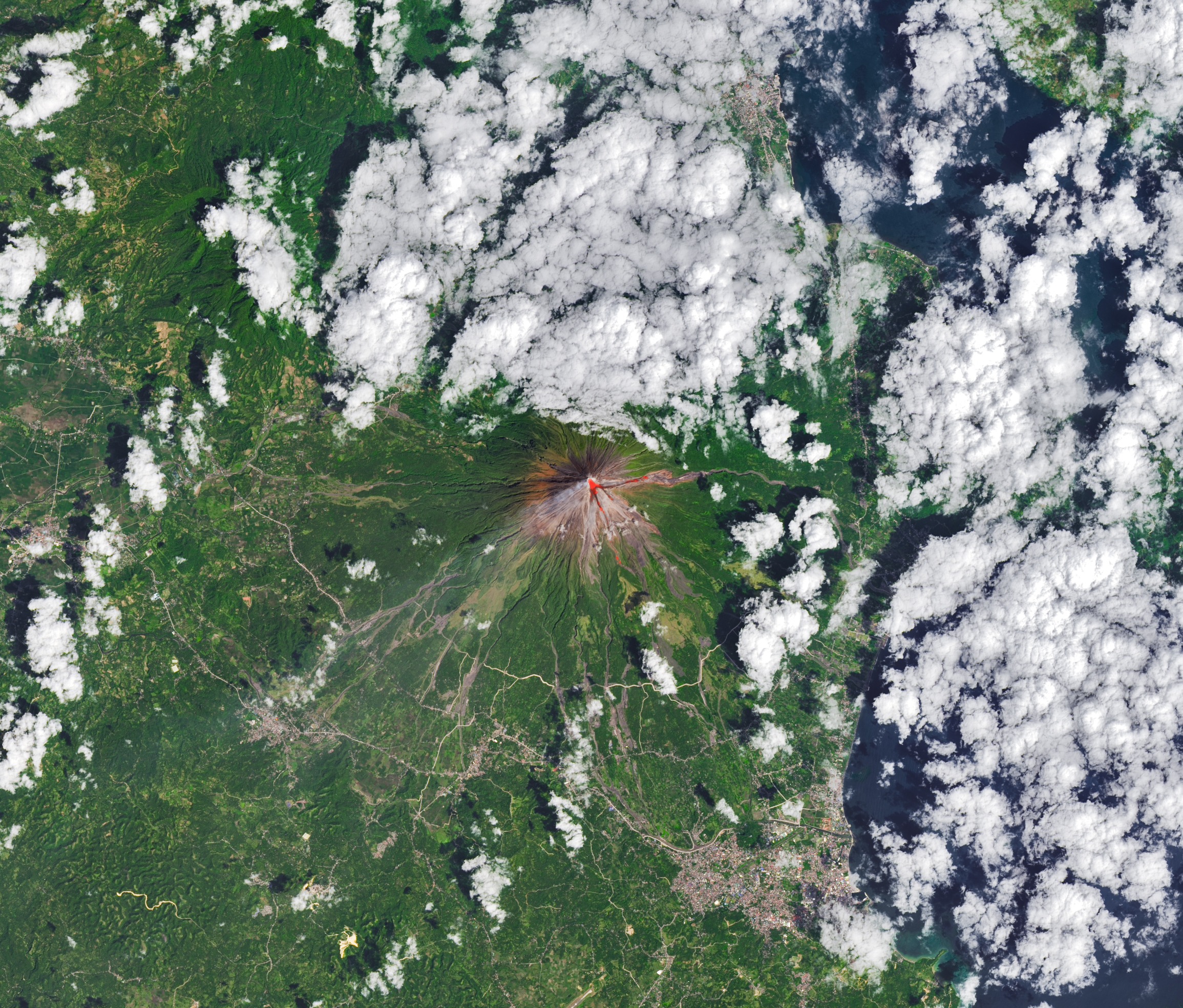 clouds float above a green landscape, in the center of which is a tall cone-shaped mountain with a bright red circle at its peak