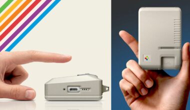 A hand points to a small, vintage computer device lying on its side. Another hand holds a similar device upright. Both devices are beige with retro design elements and colorful stripes in the background.