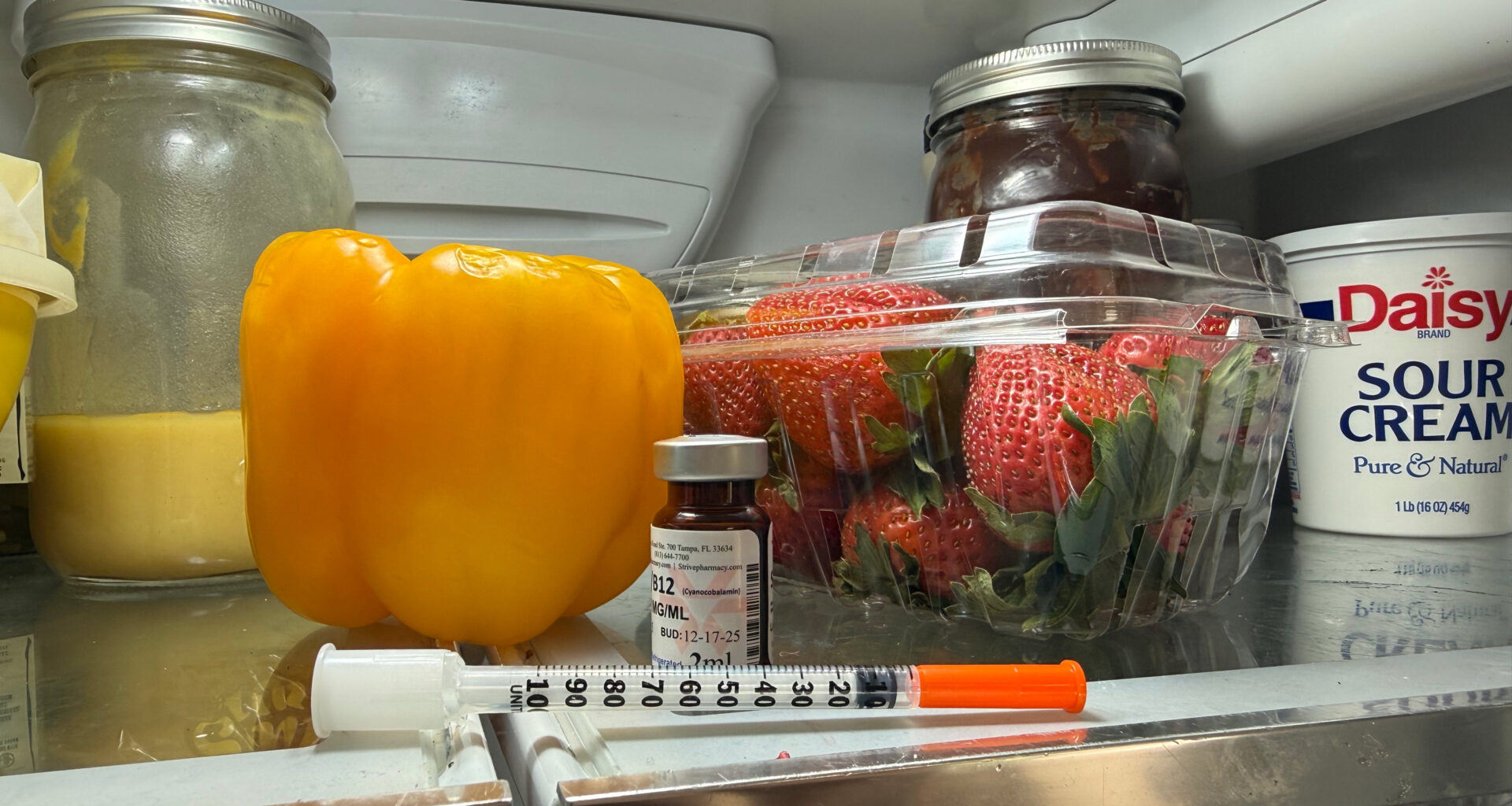 A syringe rests on the top shelf of a fridge.