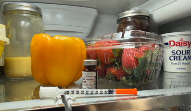 A syringe rests on the top shelf of a fridge.
