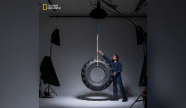 A man in a studio setting stands next to a large tire hanging from the ceiling by a rope. He is touching the tire, and professional lighting equipment is visible around him. The National Geographic logo appears in the top left corner.