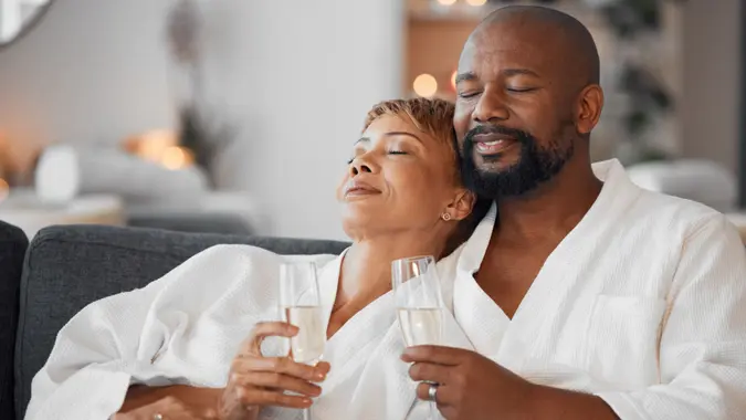 Wealthy middle class couple in robes, relaxing on a spa couch with champagne.