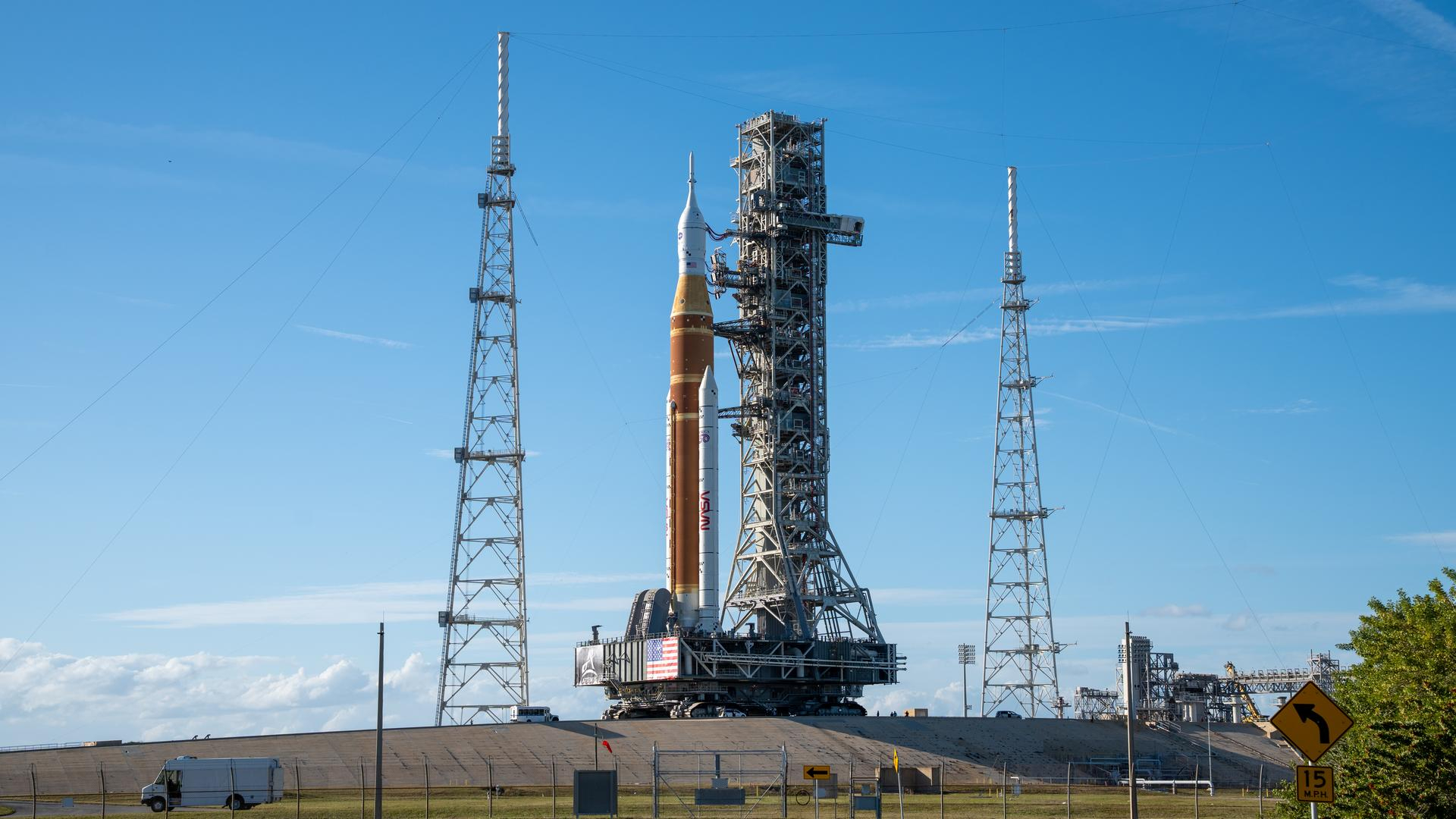a large orange and white rocket sits on a launch pad under blue skies