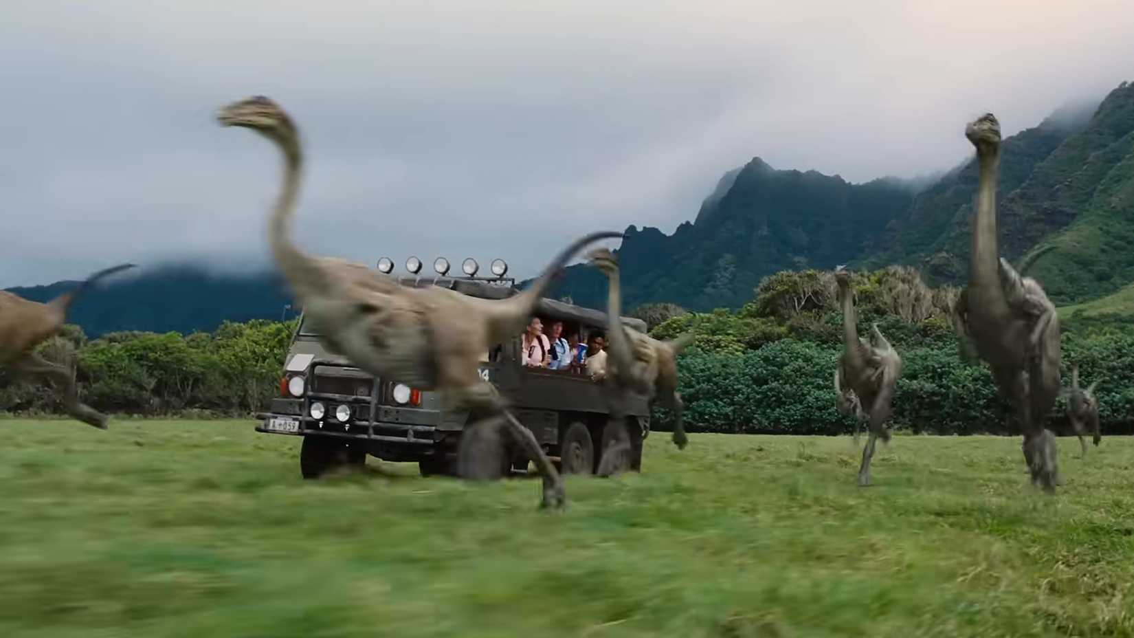 A truck full of Jurassic World guests driving alongside running herbivores
