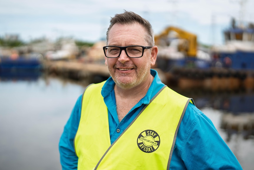 A man in a blue shirt with a bright yellow vest over the top smiles at the camera.