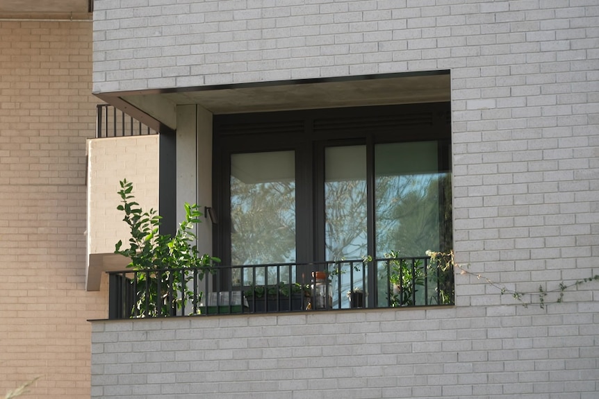 A grey brick building with a balcony with black railing.