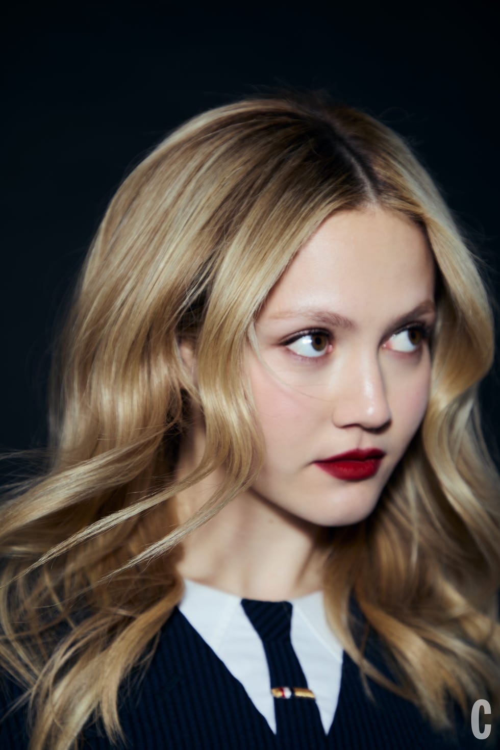 Half-portrait of a person with a blurred face, featuring long, wavy blonde hair.