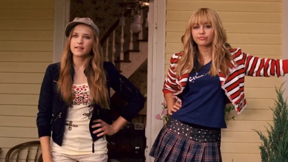  Emily Osment and Miley Cyrus as Lilly and Hannah standing on a porch in Hannah Montana: The Movie. 