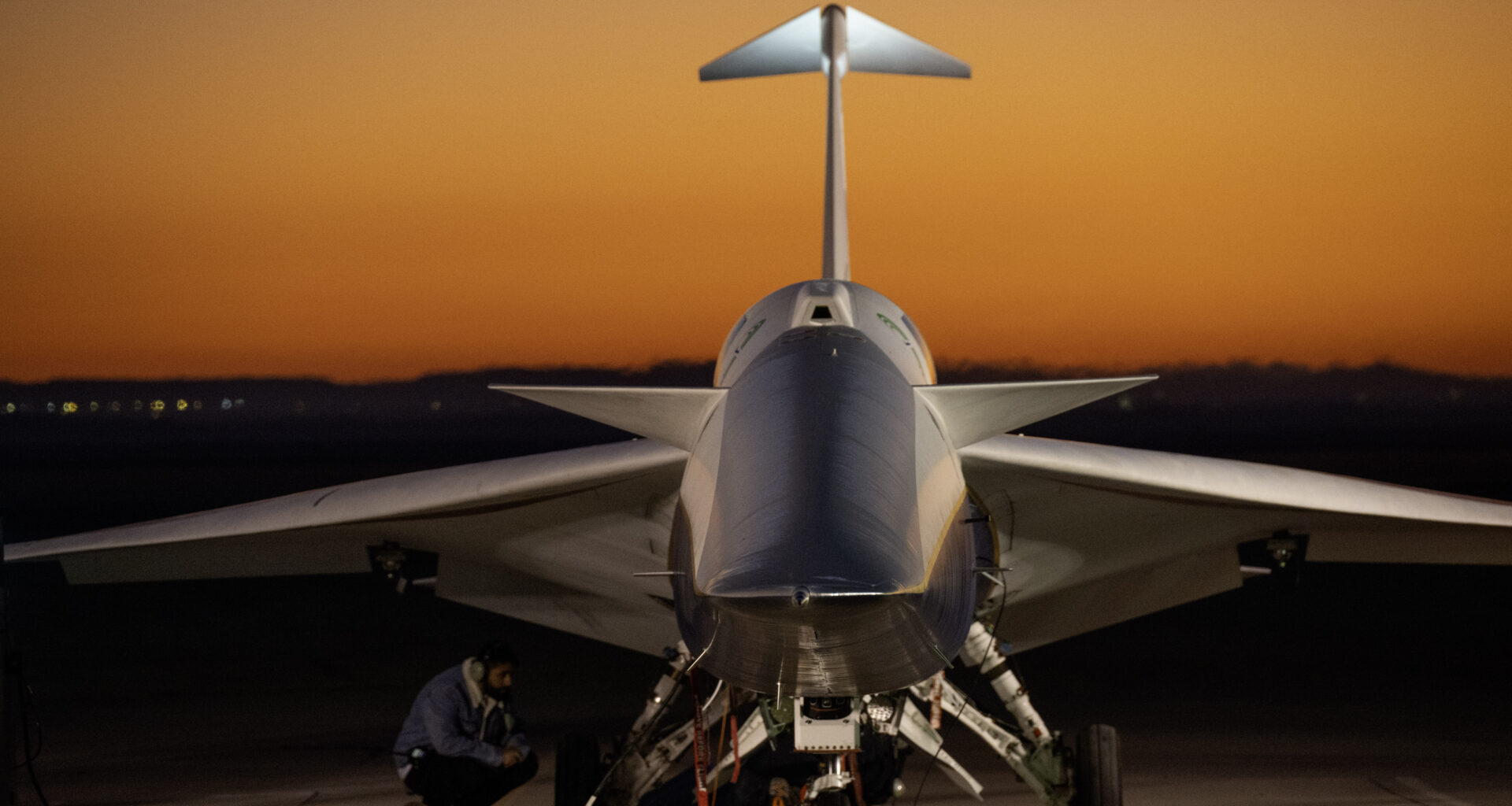 An aircraft resting on a section of runway as seen from the front, with its nose facing the camera. The early morning sky is orange in the background.