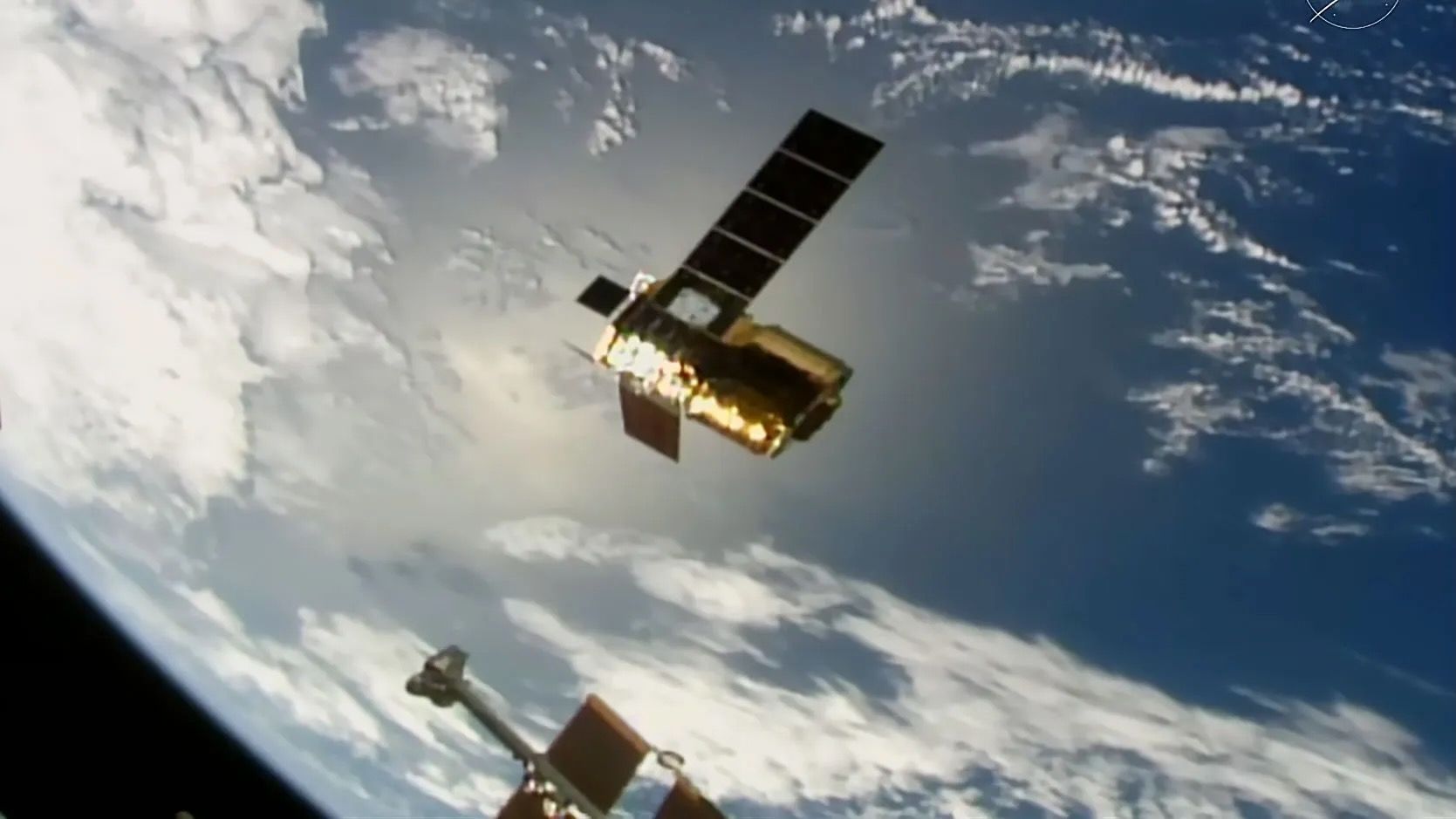 a cylindrical golden spacecraft with a pair of long, rectangular solar arrays extended is seen from above with earth in the background