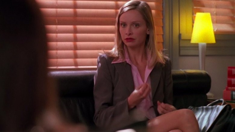 Ally McBeal (Calista Flockhart) gestures with her hands while sitting on a couch in Ally McBeal