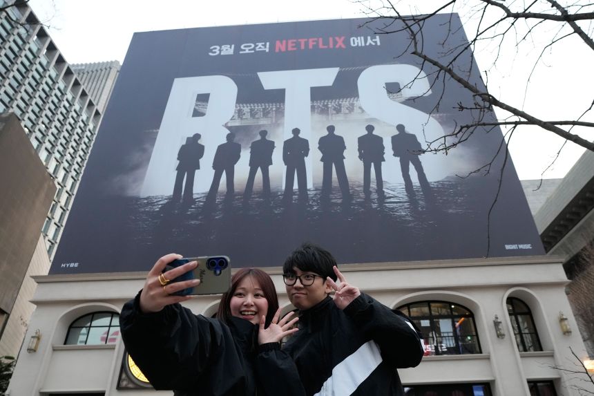 A couple takes a selfie photo near a banner promoting a comeback concert of BTS at Gwanghwamun Square in Seoul this week.