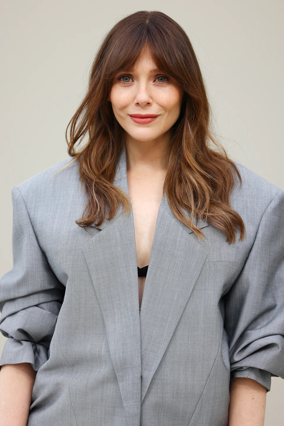 Person in oversized gray blazer with long sleeves, smiling, with loose wavy hair