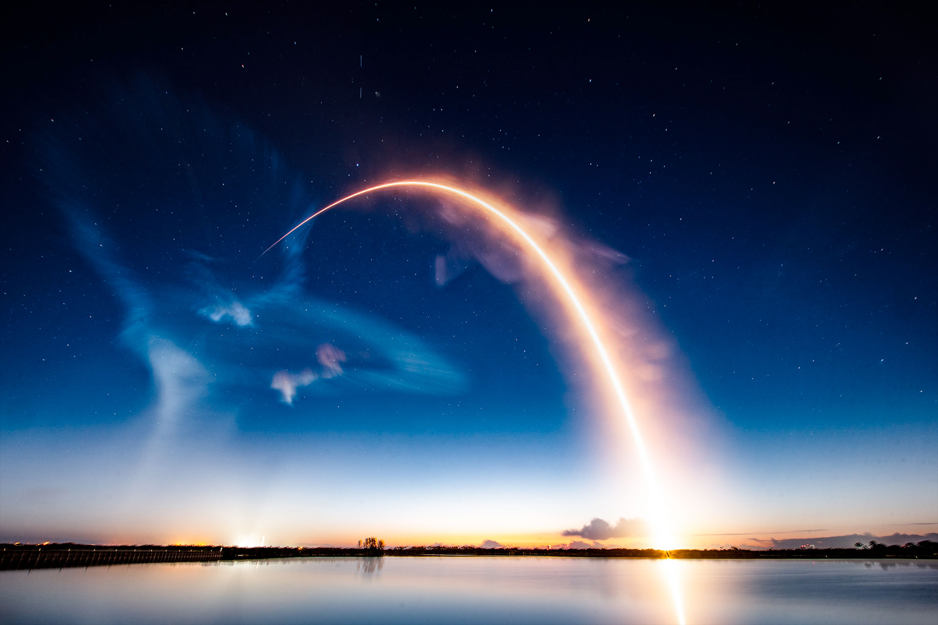 a time lapse exposure of a pre-dawn rocket launch captures its orange-white glowing streak and the jellyfish like plume it created.