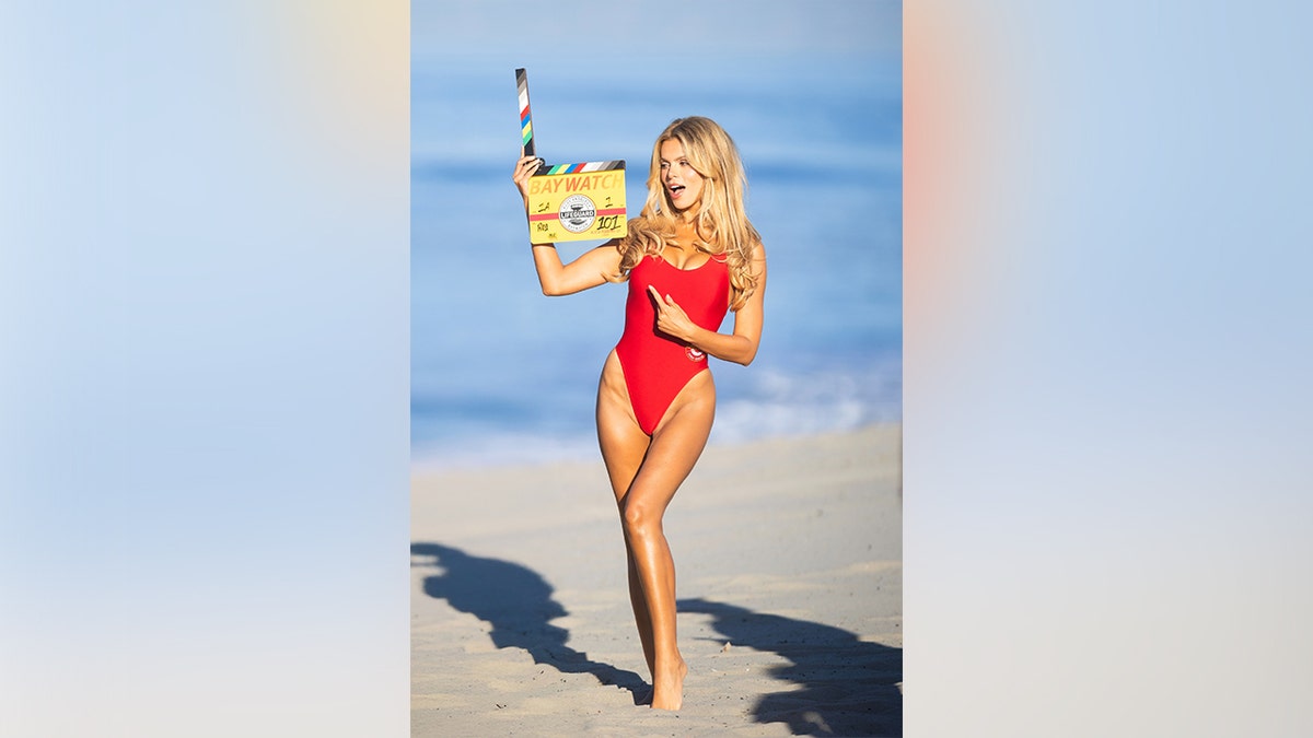Brooks Nader posing on Venice Beach in a red bikini while holding a slate in March 2026.