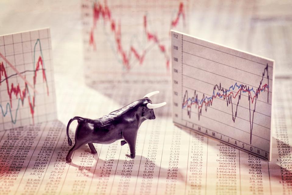 A bull figurine stands on newsprint and looks at stock price charts.
