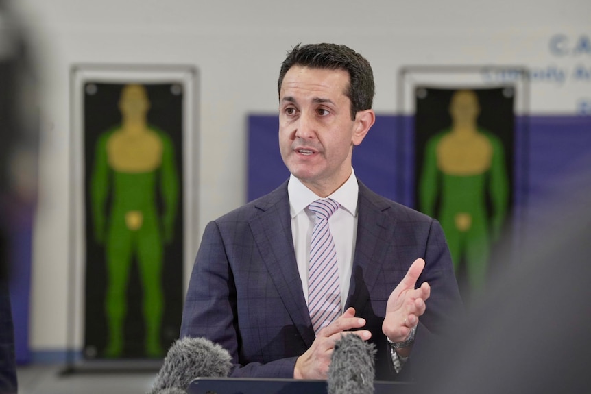 A man with dark hair, wearing a blue jacket, speaking to reporters.