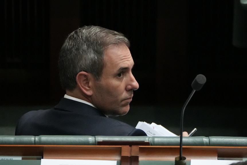 Jim Chalmers sitting down and looking behind him.