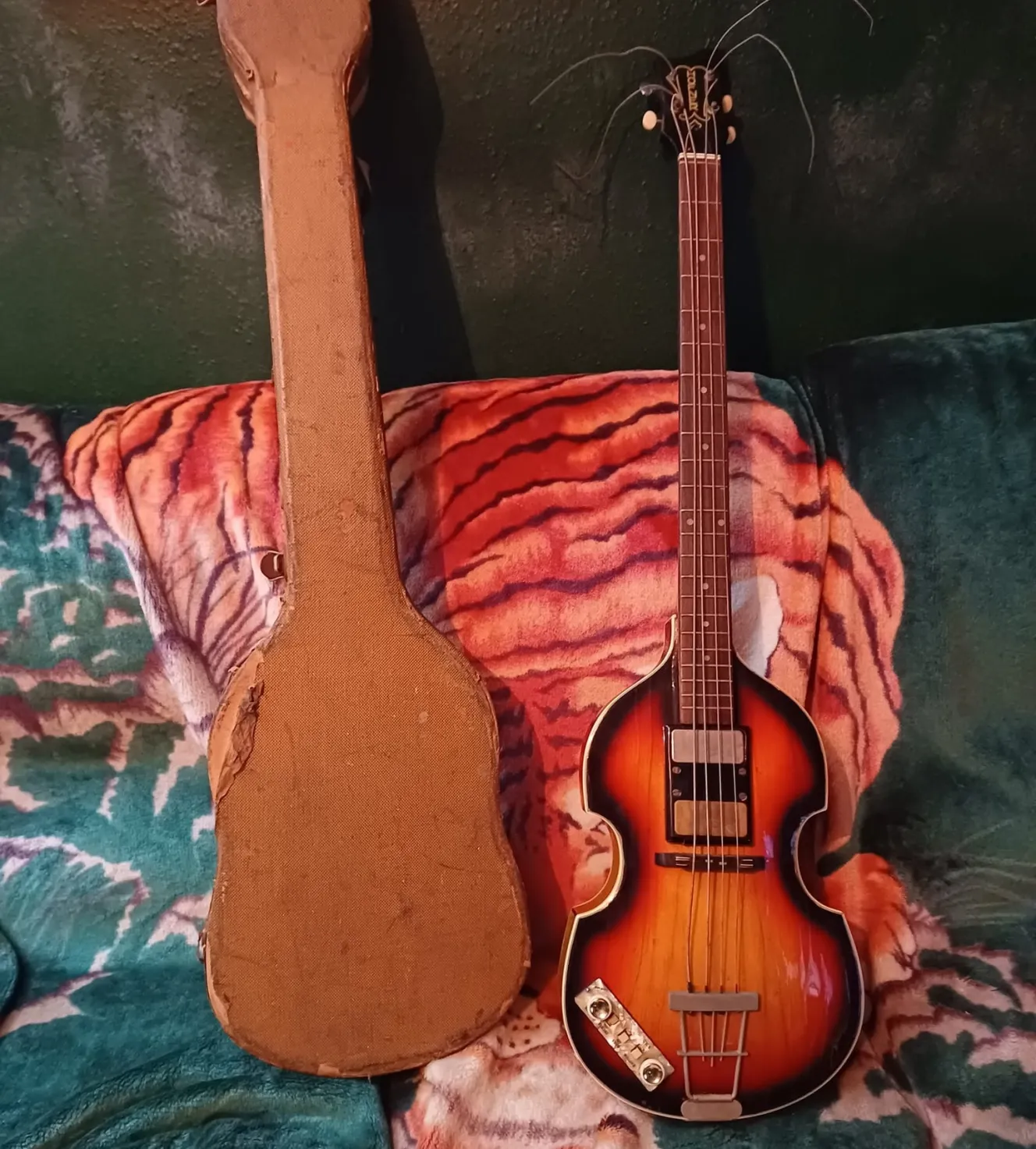 A vintage Hofner violin bass guitar and its worn case resting on a tiger-print blanket.